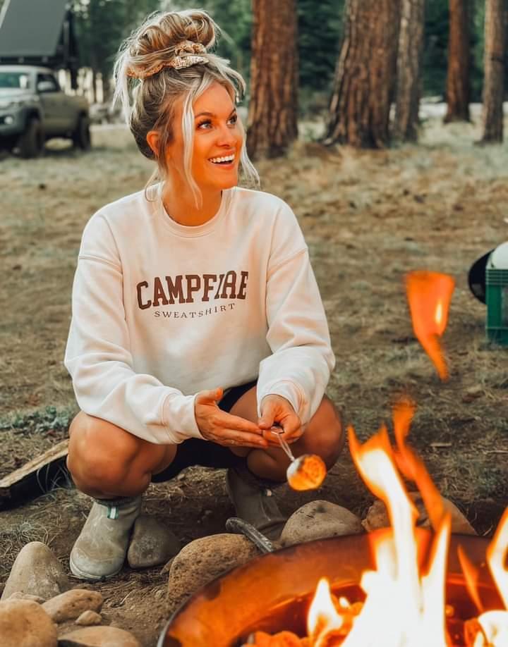A mom wearing a beige hoodie that says “campfire sweatshirt”