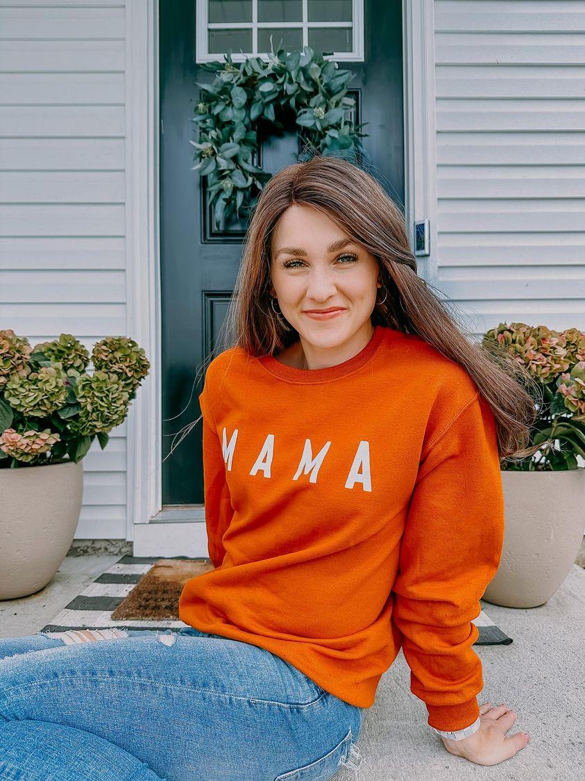 A mom wearing an orange hoodie that says “mama”
